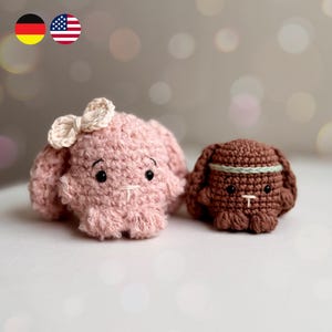 Könnte beinhalten: Zwei handgefertigte Häkelhasen-Puppen. Einer ist rosa mit einer Schleife, der andere ist braun mit einem Stirnband. Beide haben schwarze Augen und weiße Nahtdetails. Die Hasen sind klein, weich und wahrscheinlich als Spielzeug oder Dekorationsartikel gedacht.