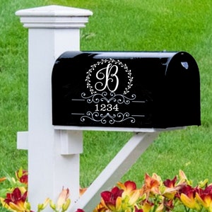 May include: A black mailbox with a white post. The mailbox features a white floral design with the letter "B" and the number "1234". The mailbox is set against a backdrop of green grass and colorful flowers.