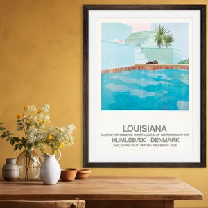Könnte beinhalten: Ein gerahmtes Poster mit einem minimalistischen Design, das einen blauen Swimmingpool und ein Gebäude im Hintergrund zeigt. Das Poster trägt den Titel "Louisiana" und enthält den Text "Museum for Moderne Kunst, Museum of Contemporary Art, Humlebæk, Denmark, Daglig Daily 10-17, Onsdag Wednesday 10-22."