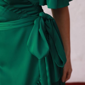 May include: A green wrap dress with a ruffled neckline and short sleeves. The dress has a tie at the waist and a ruffled hem.