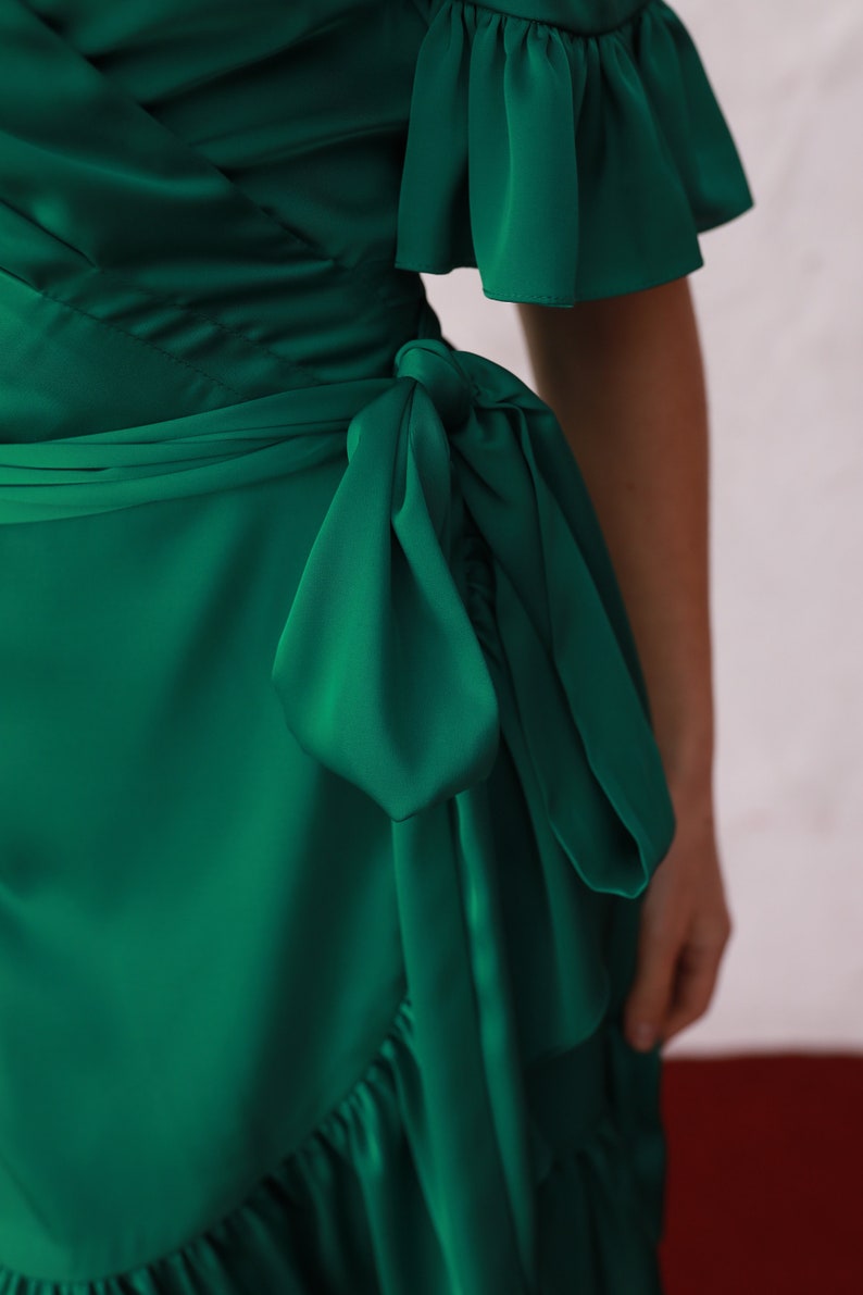 May include: A green wrap dress with a ruffled neckline and short sleeves. The dress has a tie at the waist and a ruffled hem.
