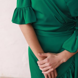 May include: A green wrap dress with a ruffled neckline and sleeves. The dress has a tie at the waist and a ruffled hem.