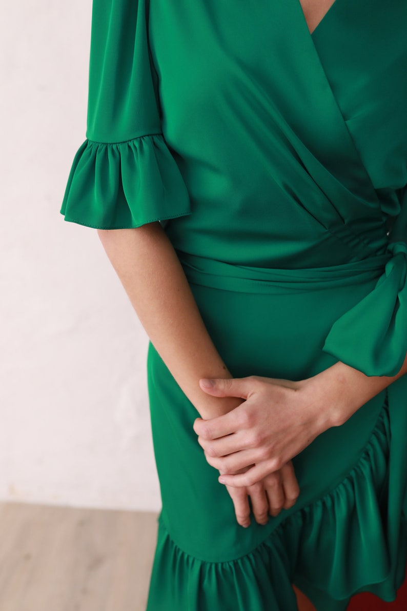 May include: A green wrap dress with a ruffled neckline and sleeves. The dress has a tie at the waist and a ruffled hem.