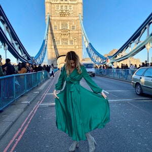 May include: A woman wearing a green satin dress and grey boots poses on Tower Bridge in London, England.