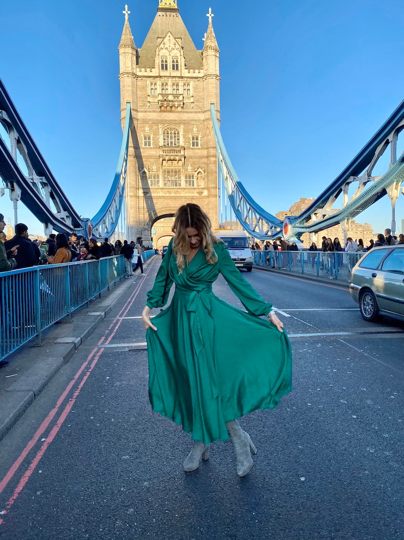 May include: A woman wearing a green satin dress and grey boots poses on Tower Bridge in London, England.