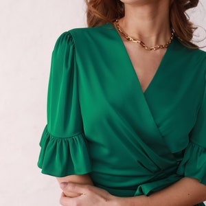 May include: A green wrap dress with a V-neckline and ruffled sleeves. The dress has a tie at the waist.