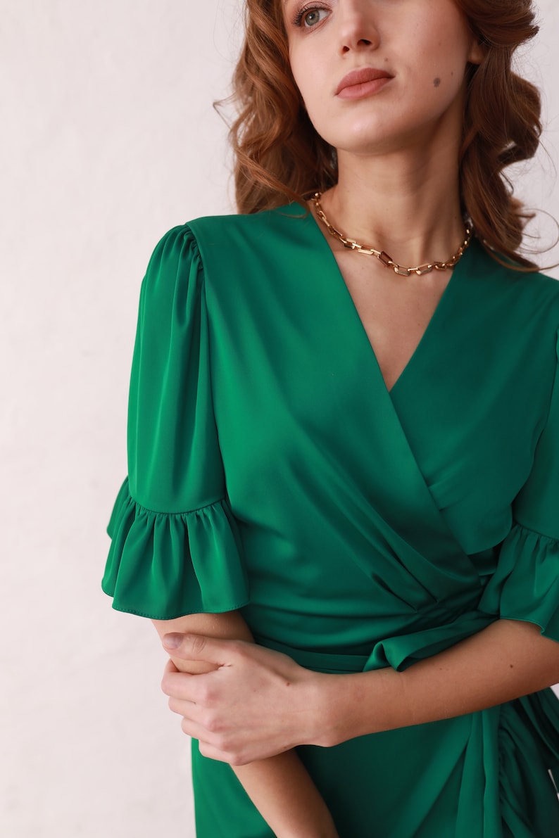 May include: A green wrap dress with a V-neckline and ruffled sleeves. The dress has a tie at the waist.