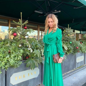May include: A woman wearing a green wrap dress with a brown purse and grey boots. She is standing in front of a building with a sign that says "The Ivy".