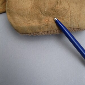 K&ouml;nnte beinhalten: Nahaufnahme eines braunen Ledermaterials mit einem kleinen Loch in der Mitte. Das Material ist strukturiert und weist eine leicht abgenutzte Optik auf.