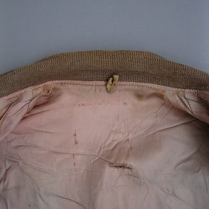 K&ouml;nnte beinhalten: Das Innere einer braunen Jacke mit einem rosa Futter. Das Futter hat ein kleines Loch in der Mitte und ein paar weitere kleine L&ouml;cher an den R&auml;ndern.