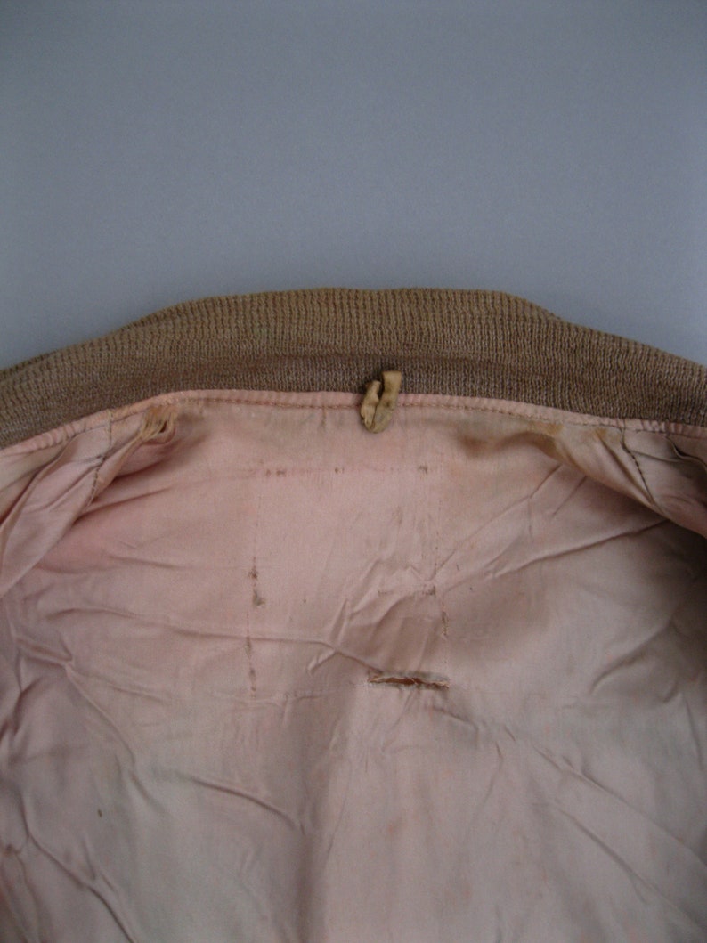 K&ouml;nnte beinhalten: Das Innere einer braunen Jacke mit einem rosa Futter. Das Futter hat ein kleines Loch in der Mitte und ein paar weitere kleine L&ouml;cher an den R&auml;ndern.