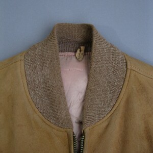 K&ouml;nnte beinhalten: Eine braune Wildlederbomberjacke mit einem braunen gerippten Strickkragen und einem Rei&szlig;verschluss.