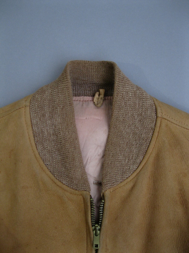 K&ouml;nnte beinhalten: Eine braune Wildlederbomberjacke mit einem braunen gerippten Strickkragen und einem Rei&szlig;verschluss.