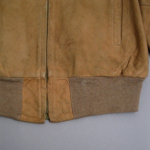 K&ouml;nnte beinhalten: Eine braune Wildlederbomberjacke mit Rei&szlig;verschluss und einem gerippten Strickbund.
