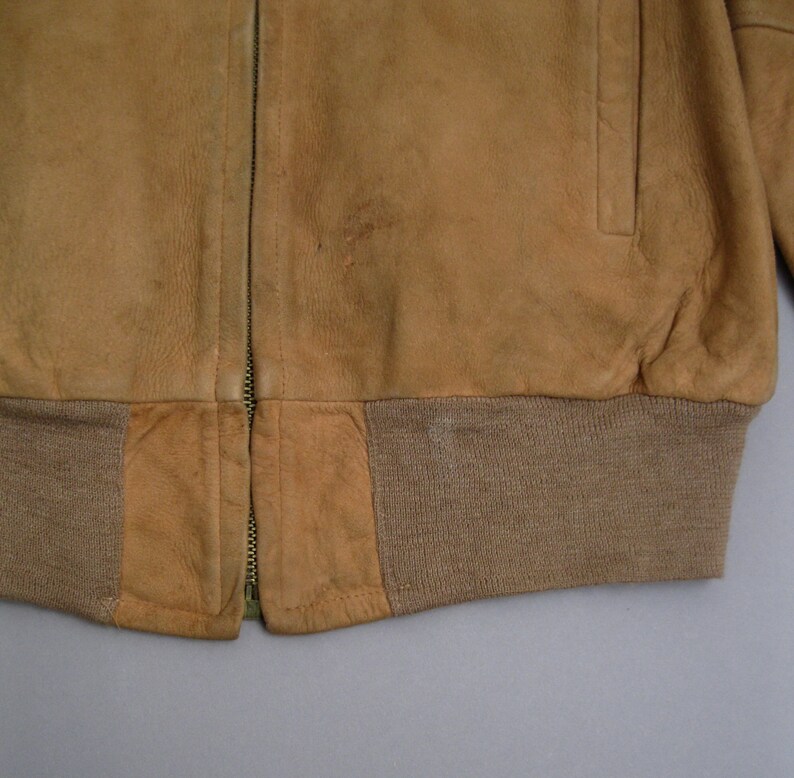 K&ouml;nnte beinhalten: Eine braune Wildlederbomberjacke mit Rei&szlig;verschluss und einem gerippten Strickbund.