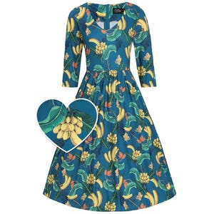 May include: A teal knee-length dress featuring a repeating pattern of yellow bananas and green tropical leaves. The dress has three-quarter length sleeves, a round neckline, and a fitted bodice that flares into a pleated skirt. A heart-shaped inset shows a detail of the banana print.