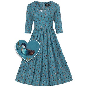 Puede incluir: Un vestido azul turquesa con estampado de patos. El vestido tiene cuello en V y mangas 3/4. El estampado de patos es de estilo acuarela y presenta un pato nadando en un estanque con juncos.