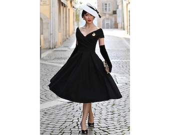 May include: A black vintage-style dress with a flared skirt, off-the-shoulder neckline, and a small gold brooch. The outfit includes long black gloves, a white hat with a black bow, and black heels. A gold clutch is held.