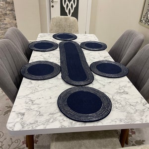 May include: A white marble dining table with six chairs. The table is set with a blue and silver table runner and six matching placemats.