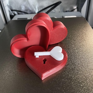 May include: A red heart-shaped box with a white heart-shaped key inside. The box is open and the key is visible.