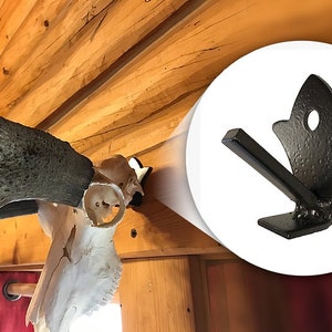 May include: Black metal antler mount with a decorative, pointed design. The mount is attached to a wooden beam.
