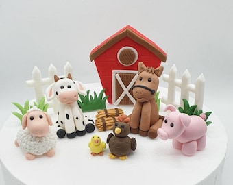 May include: A set of farm animal cake toppers, including a cow, horse, pig, sheep, chick, and a red barn with a white picket fence. The animals are made of fondant and are in various colors, including white, brown, pink, and yellow.
