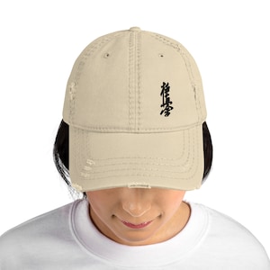 May include: A beige distressed baseball cap with black embroidered kanji characters. The characters are "karate" in Japanese.