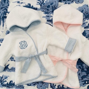 May include: Two white hooded bathrobes with blue and pink striped trim. One robe has a blue striped sash and the other has a pink striped sash. The robe on the left has the monogram "JGD" embroidered on the front.