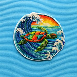 Peut inclure: Écusson brodé circulaire représentant une tortue de mer nageant devant une vague. La carapace de la tortue est un mélange vibrant d'orange, de vert et de bleu. La vague est bleue et blanche, avec un coucher de soleil en arrière-plan.