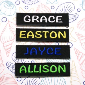 May include: Four black fabric name tags with white, yellow, blue, and green embroidered lettering. The names are "GRACE", "EASTON", "JAYCE", and "ALLISON".