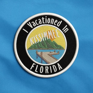 Może przedstawiać: Haftowana naszywka z napisem "I Vacationed In Kissimmee Florida". Naszywka ma okrągły kształt z krajobrazem molo, gór i słońca. Naszywka jest czarna, biała, żółta, zielona i niebieska.