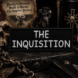 May include: A black rectangular patch with the words "THE INQUISITION" embroidered in white. The patch is displayed with a skull, miniature figurines, and a scroll with text.