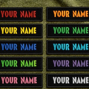 May include: A collection of embroidered name patches with the text "YOUR NAME" in various colors, including red, orange, yellow, green, blue, teal, purple, pink, and white. The patches are rectangular with black borders and are displayed on a textured green background.