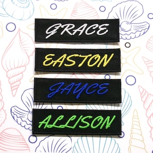Puede incluir: Cuatro parches de tela negra con letras bordadas en blanco, amarillo, azul y verde. Los parches dicen "GRACE", "EASTON", "JAYCE" y "ALLISON".