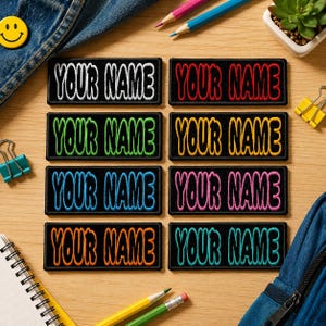 May include: Eight rectangular black embroidered patches featuring the text YOUR NAME in different colors including white, red, green, yellow, blue, pink, orange, and teal. Each patch has a thick black border and bold, stylized lettering.
