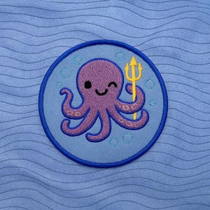 Peut inclure: Écusson brodé représentant une pieuvre violette tenant un trident jaune. La pieuvre sourit et fait un clin d'œil, entourée de bulles, sur un fond bleu clair avec une bordure bleu foncé. L'écusson est circulaire.