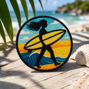 May include: Round embroidered patch featuring a black silhouette of a person carrying a yellow surfboard on a beach. The patch has a blue border with a beach scene, including waves, sand, and a sunset. The background shows a beach and ocean.