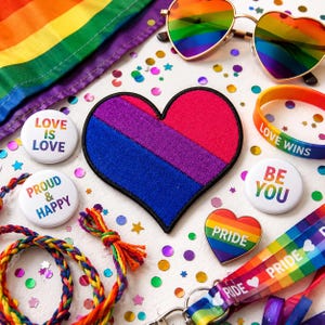 May include: A heart-shaped patch with pink, purple, and blue stripes, surrounded by rainbow-colored accessories including heart-shaped sunglasses, a wristband with "LOVE WINS" text, buttons with "LOVE IS LOVE" and "BE YOU" text, and a lanyard.