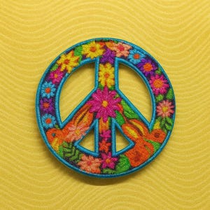 K&ouml;nnte beinhalten: Gestickter Peace-Zeichen-Aufn&auml;her mit t&uuml;rkisfarbenem Umriss, gef&uuml;llt mit bunten Blumen in Rosa-, Gelb-, Orange- und Lilat&ouml;nen. Der Aufn&auml;her befindet sich auf einem gelben, strukturierten Hintergrund.