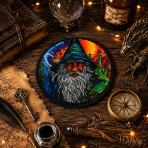 May include: A circular embroidered patch featuring a detailed portrait of a wizard with a long white beard and a pointed hat. The design incorporates vibrant colors including blue, orange, and green, with a black border surrounding the artwork.