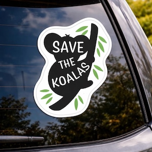May include: A white sticker with a black silhouette of a koala bear clinging to a branch, with green leaves. The text "SAVE THE KOALAS" is in white. The sticker is affixed to a car window.