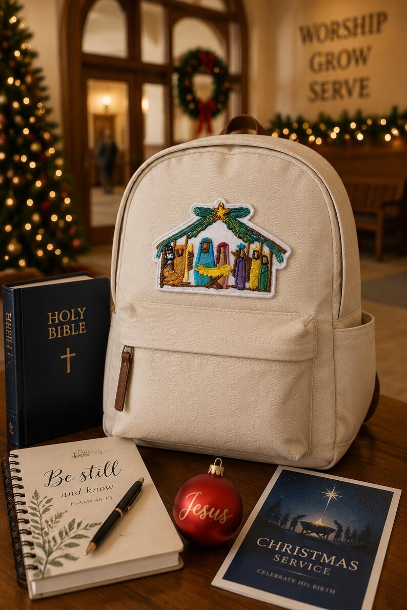May include: A beige canvas backpack featuring an embroidered nativity scene patch. The backpack is displayed alongside a black Holy Bible, a spiral-bound notebook with the text Be still and know, a red ornament with the word Jesus, and a card.