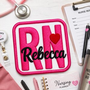 May include: A square embroidered patch with a white background and a hot pink border. The patch features large hot pink letters spelling RN with a small red heart, and the name Rebecca in black script. It is surrounded by nursing supplies.