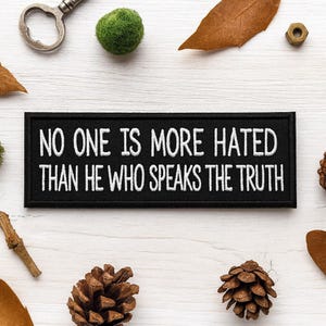 以下が含まれることがあります： NO ONE IS MORE HATED THAN HE WHO SPEAKS THE TRUTHという白い刺繍文字が施された、長方形の黒い刺繍ワッペン。ワッペンにはきれいな縁取りが施されており、ジャケットやバッグなどの布製品に取り付けられるように設計されています。
