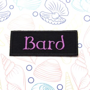 Pode incluir: Remendo de tecido preto com a palavra "Bard" bordada em rosa.