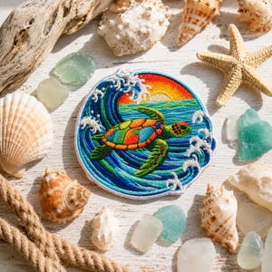 Puede incluir: Un parche bordado circular que presenta una tortuga marina colorida nadando a través de olas oceánicas azules con espuma blanca. El fondo muestra un sol vibrante de color naranja y amarillo poniéndose sobre el agua, en bordado detallado.
