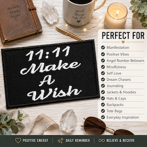 May include: A rectangular black embroidered patch featuring the white text 11:11 Make A Wish. The patch is displayed alongside a brown journal with the text Manifest Believe Receive, a mug, a candle, a gold pen, and sunglasses on a light surface.