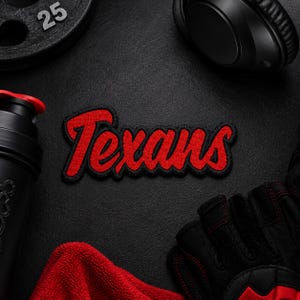 Op de afbeelding: Een rood en zwart geborduurd embleem met het woord "Texans" in een scriptlettertype. Het embleem is omgeven door trainingsapparatuur, waaronder een gewichtplaat, een koptelefoon, een shakerfles, een handdoek en trainingshandschoenen.
