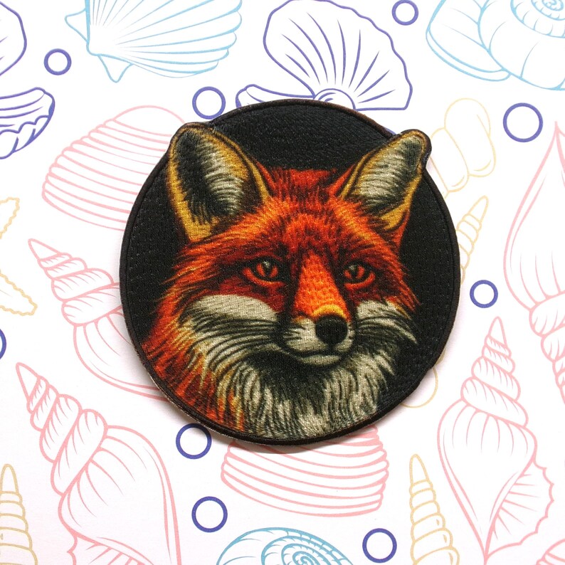 Peut inclure: Un patch rond brod&eacute; repr&eacute;sentant une image d&eacute;taill&eacute;e du visage d'un renard roux sur un fond noir.