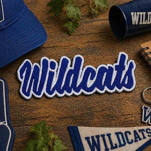 May include: A collection of blue and white Wildcats themed merchandise, including a baseball cap, a patch, a keychain, a pennant, and a foam finger. The word "Wildcats" is prominently displayed on several items.